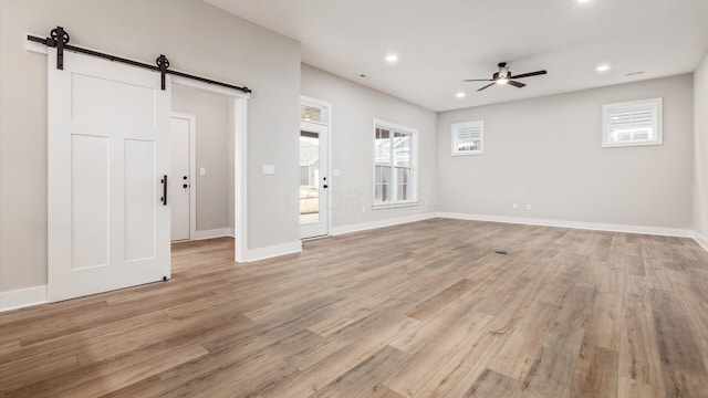 interior space with ceiling fan, a barn door, and light hardwood / wood-style floors