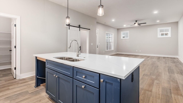 kitchen featuring pendant lighting, sink, blue cabinetry, a center island with sink, and a barn door