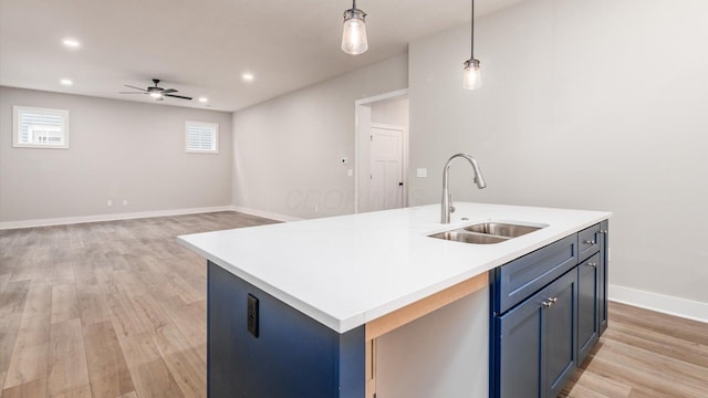 kitchen with blue cabinets, sink, a center island with sink, light wood-type flooring, and pendant lighting