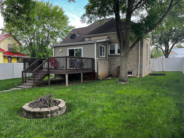 rear view of house with a fire pit, a deck, and a lawn