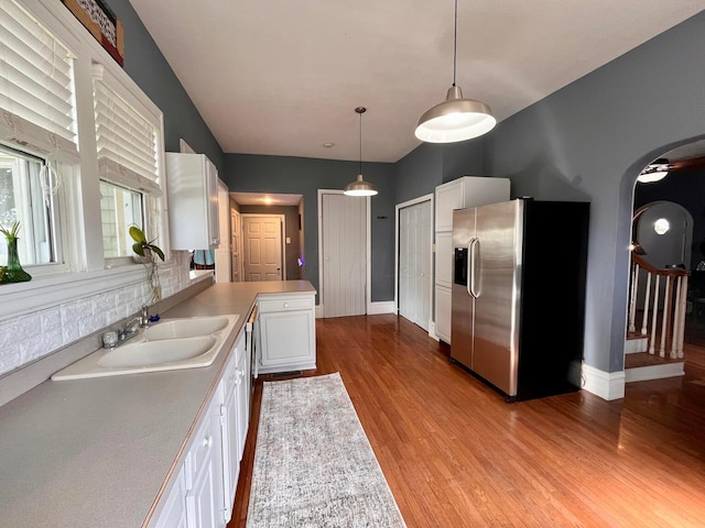 kitchen with stainless steel fridge, light wood-type flooring, sink, white cabinets, and hanging light fixtures