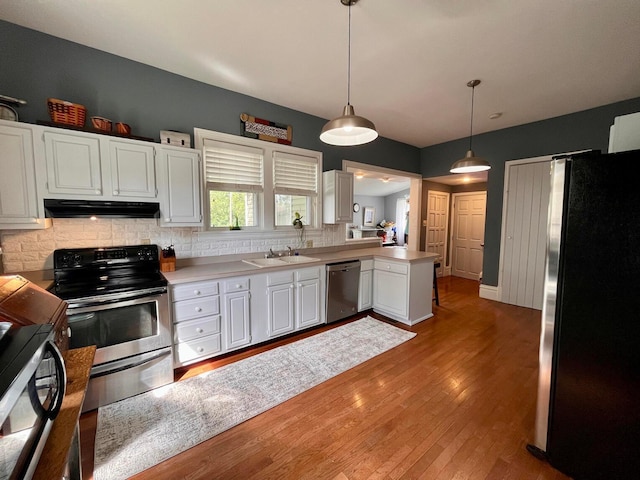 kitchen with hardwood / wood-style floors, white cabinets, sink, appliances with stainless steel finishes, and decorative light fixtures