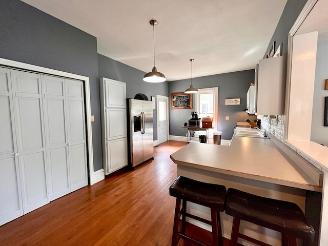 kitchen featuring a kitchen breakfast bar, stainless steel refrigerator with ice dispenser, kitchen peninsula, hardwood / wood-style floors, and decorative light fixtures