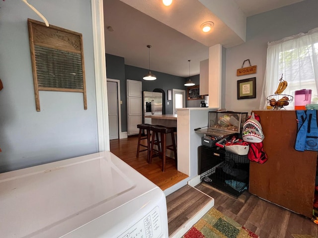 kitchen featuring a kitchen bar, kitchen peninsula, dark wood-type flooring, pendant lighting, and washer / dryer