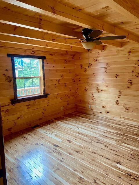 spare room featuring beamed ceiling, hardwood / wood-style floors, wooden walls, and wood ceiling