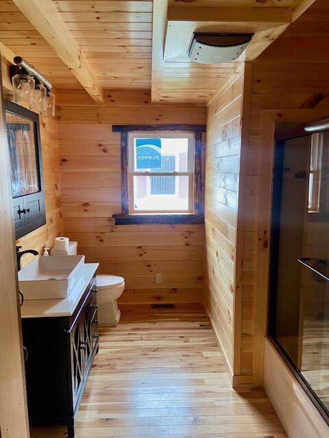 full bathroom with wood-type flooring, vanity, and wood walls