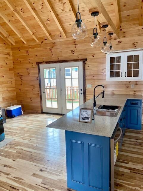 kitchen with lofted ceiling with beams, blue cabinets, wood walls, decorative light fixtures, and light wood-type flooring