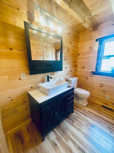 bathroom with wooden walls, hardwood / wood-style floors, and beamed ceiling