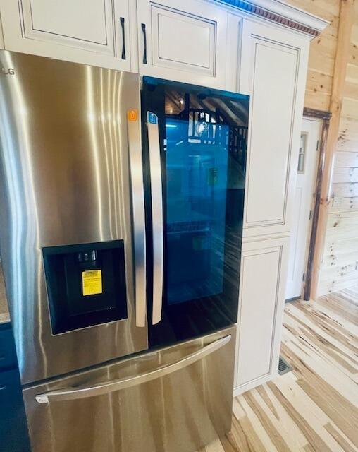 interior details with stainless steel fridge, light wood-type flooring, white cabinetry, and wooden walls