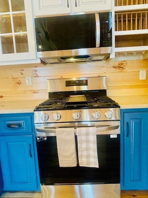 kitchen with white cabinets, appliances with stainless steel finishes, blue cabinets, and wood walls