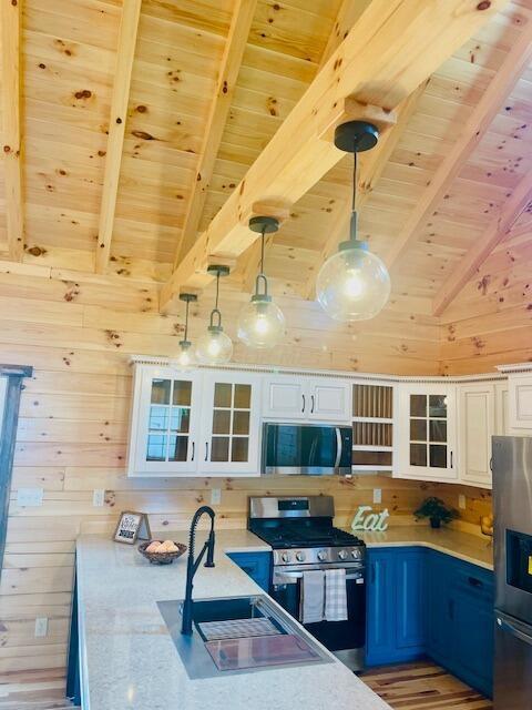 kitchen with blue cabinetry, stainless steel appliances, lofted ceiling with beams, pendant lighting, and white cabinets