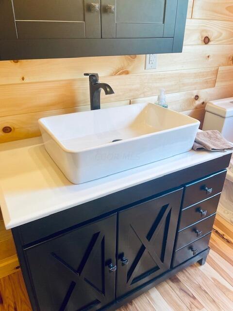 bathroom featuring wood-type flooring, vanity, toilet, and wood walls