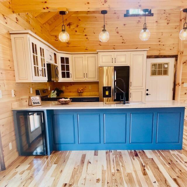 kitchen featuring wood walls, sink, decorative light fixtures, light hardwood / wood-style floors, and stainless steel appliances