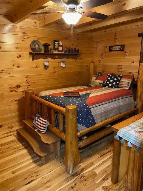 bedroom featuring wooden walls, beamed ceiling, and wood finished floors