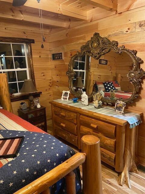 bedroom featuring beam ceiling, wood walls, and wood finished floors