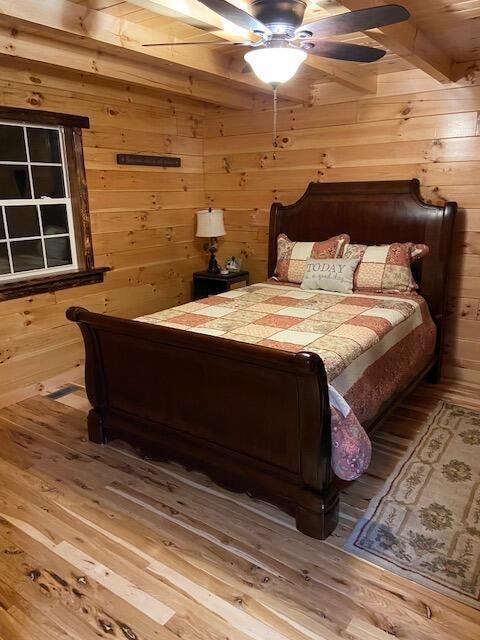 bedroom with hardwood / wood-style flooring, ceiling fan, and wood walls