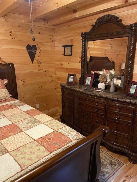 bedroom with light wood-style flooring, beam ceiling, and wooden walls