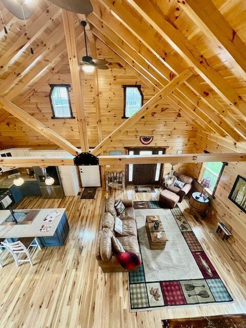 living area with vaulted ceiling with beams, a ceiling fan, wood ceiling, and wood walls