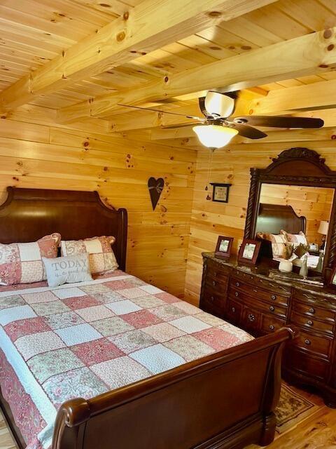bedroom with wooden walls, beamed ceiling, wood ceiling, and wood finished floors