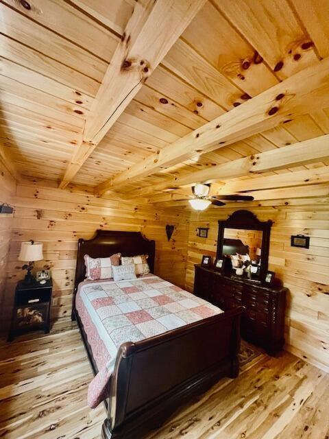 bedroom featuring light wood-style floors, wooden walls, wooden ceiling, and beamed ceiling