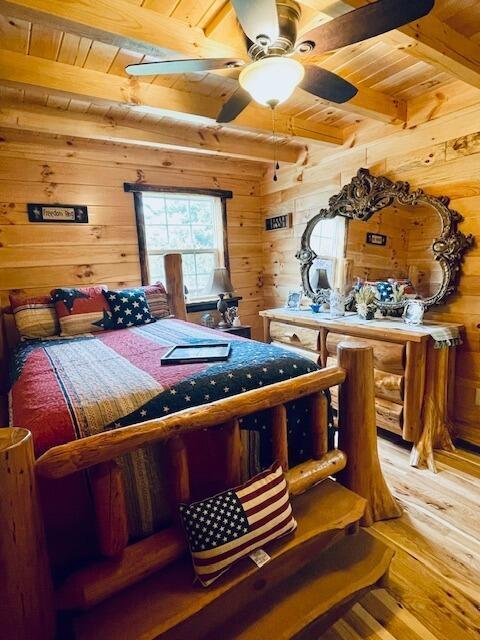 bedroom featuring light wood-style floors, wood ceiling, wood walls, and beam ceiling