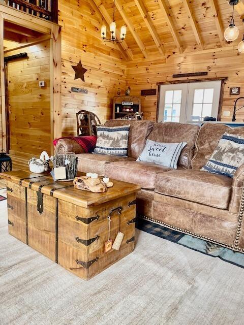 living area with lofted ceiling with beams, a chandelier, wooden walls, and wooden ceiling