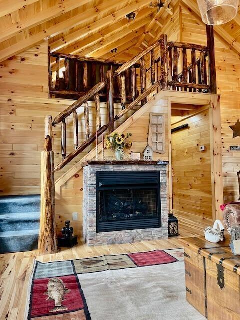 unfurnished living room featuring wood walls, a stone fireplace, wood finished floors, and stairway
