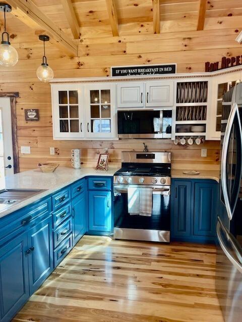 kitchen with wooden walls, appliances with stainless steel finishes, blue cabinets, and beam ceiling