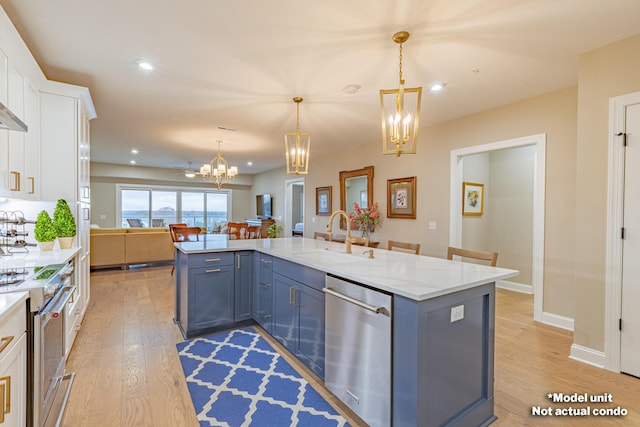 kitchen featuring white cabinetry, sink, hanging light fixtures, appliances with stainless steel finishes, and light wood-type flooring