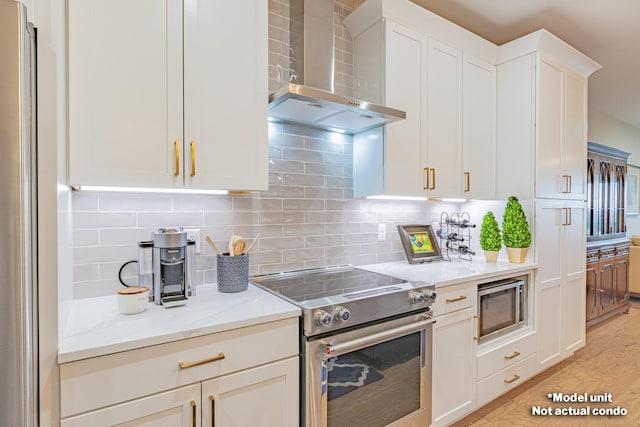 kitchen featuring white cabinetry, wall chimney range hood, tasteful backsplash, light hardwood / wood-style floors, and appliances with stainless steel finishes