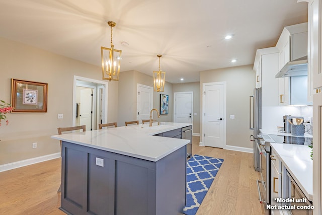 kitchen featuring a center island with sink, white cabinets, hanging light fixtures, stainless steel stove, and light hardwood / wood-style floors