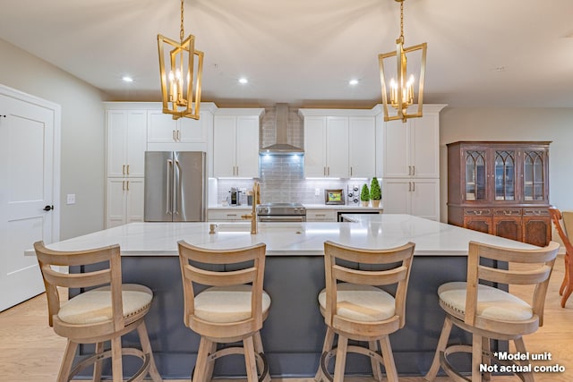 kitchen featuring light wood-type flooring, a spacious island, wall chimney range hood, and appliances with stainless steel finishes