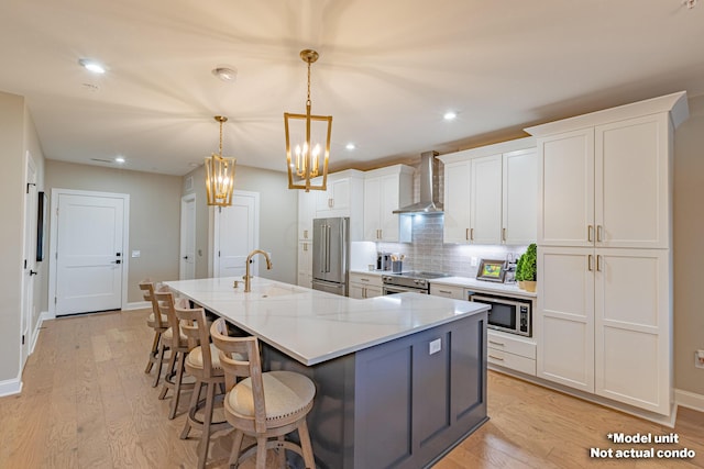 kitchen featuring a center island with sink, wall chimney range hood, appliances with stainless steel finishes, light stone counters, and white cabinetry