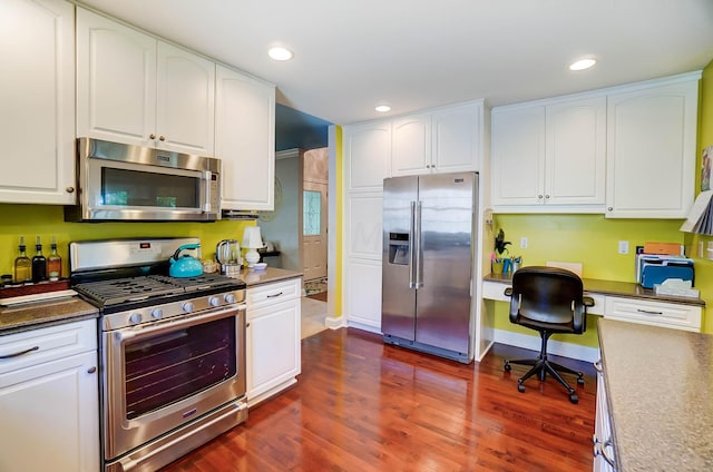 kitchen with built in desk, white cabinets, stainless steel appliances, and dark hardwood / wood-style floors