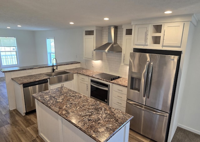 kitchen featuring kitchen peninsula, appliances with stainless steel finishes, wall chimney exhaust hood, sink, and dark hardwood / wood-style floors