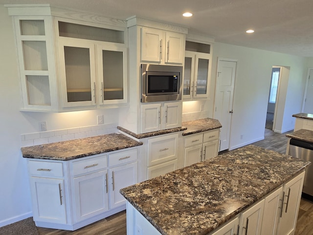 kitchen with stainless steel appliances, a kitchen island, dark hardwood / wood-style floors, dark stone counters, and white cabinets