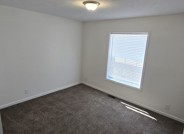 spare room with dark colored carpet and a textured ceiling