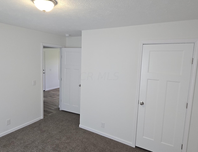 spare room featuring dark colored carpet and a textured ceiling