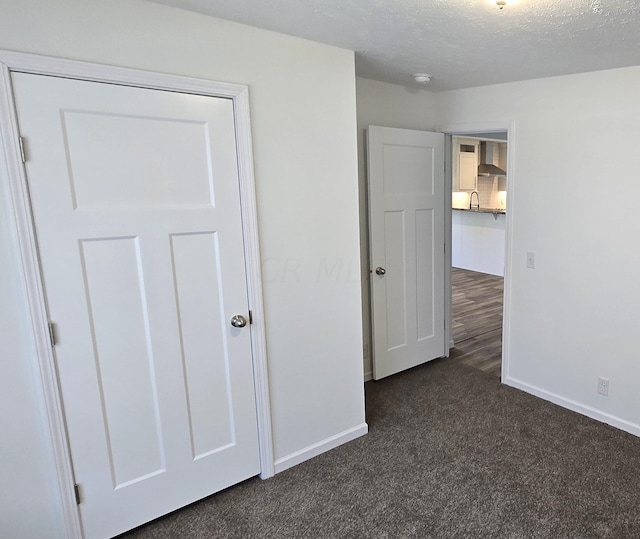 unfurnished bedroom with a textured ceiling, dark carpet, a closet, and sink