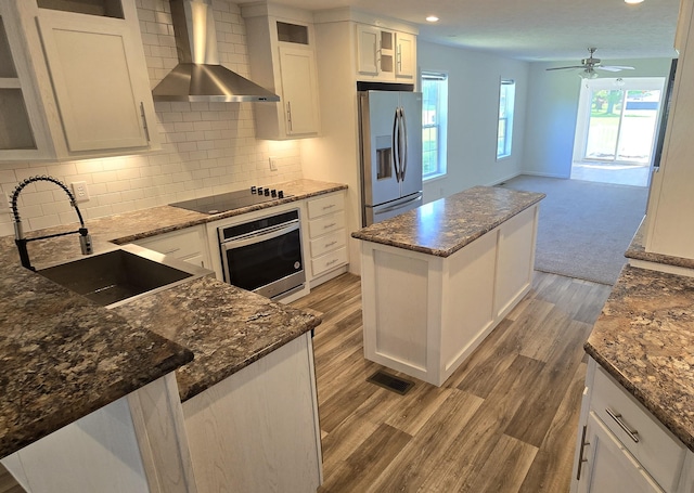 kitchen with white cabinetry, sink, wall chimney range hood, a kitchen island, and appliances with stainless steel finishes