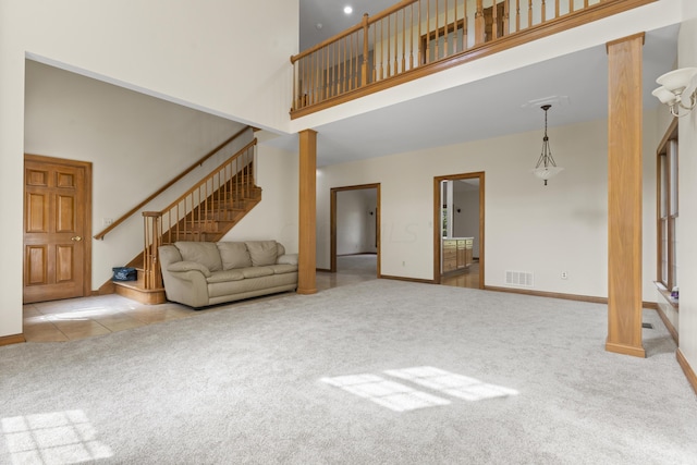 unfurnished living room featuring ornate columns, light colored carpet, and a high ceiling