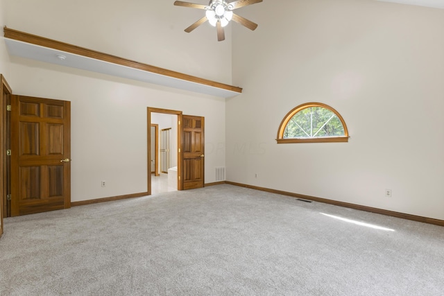 carpeted empty room featuring a towering ceiling and ceiling fan