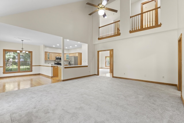 unfurnished living room with high vaulted ceiling, light colored carpet, and ceiling fan with notable chandelier