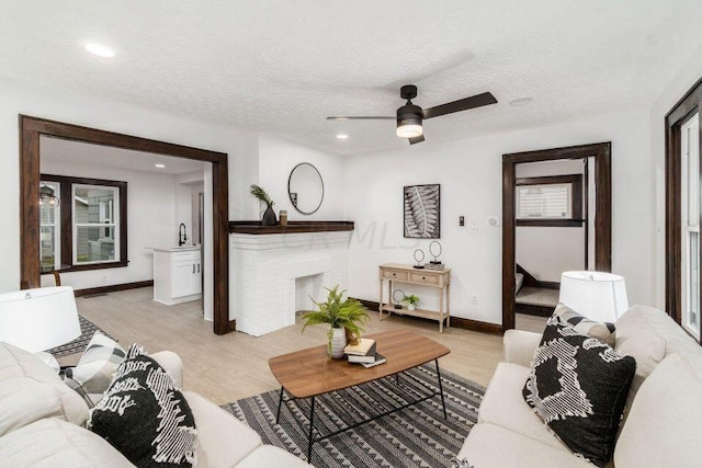 living room with light wood-type flooring, a textured ceiling, ceiling fan, and sink