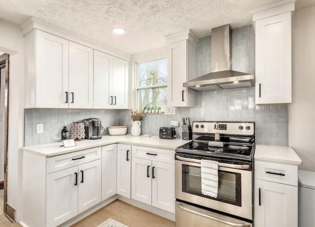 kitchen with white cabinetry, wall chimney exhaust hood, light hardwood / wood-style flooring, a textured ceiling, and stainless steel electric stove