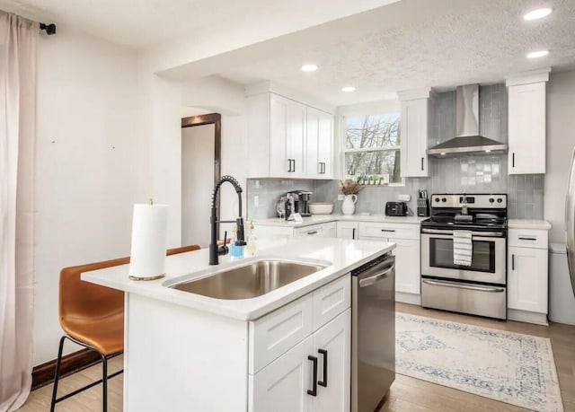 kitchen featuring appliances with stainless steel finishes, wall chimney exhaust hood, a breakfast bar, light hardwood / wood-style floors, and white cabinetry