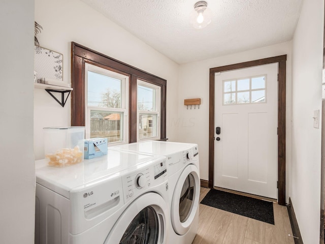 laundry room featuring light wood-type flooring, a textured ceiling, and washing machine and clothes dryer