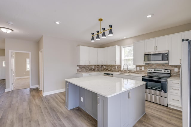 kitchen with white cabinetry, sink, stainless steel appliances, decorative light fixtures, and a kitchen island