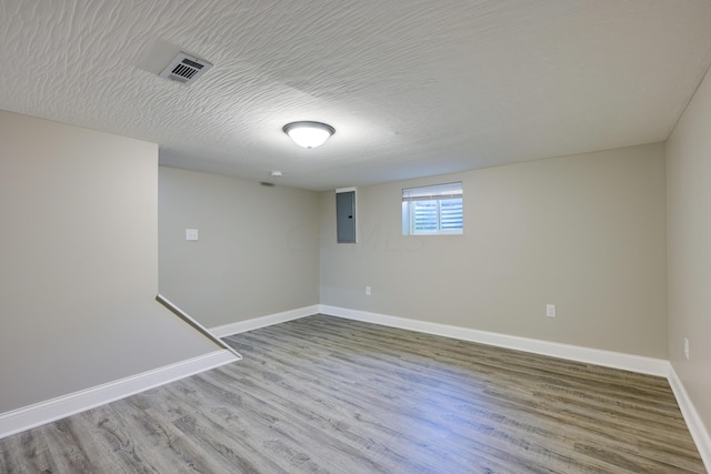 basement with wood-type flooring, a textured ceiling, and electric panel