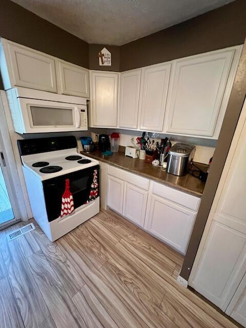 kitchen with a textured ceiling, white cabinetry, white appliances, and light wood-type flooring